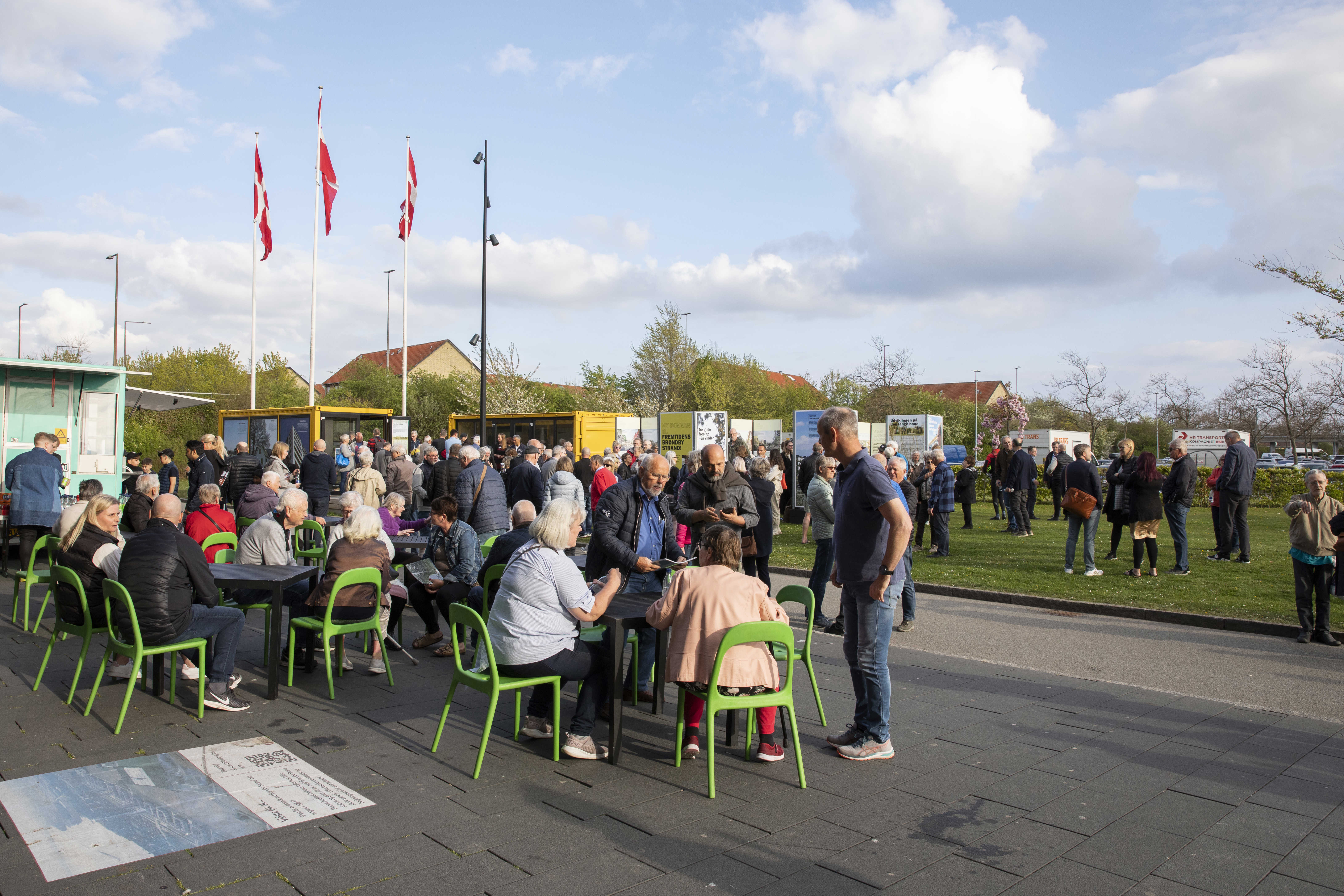 Borgere sidder og står i området mellem Brønden og Strandboxen, i baggrunden ses udstillingen af forslagene til udviklingsplanen. 